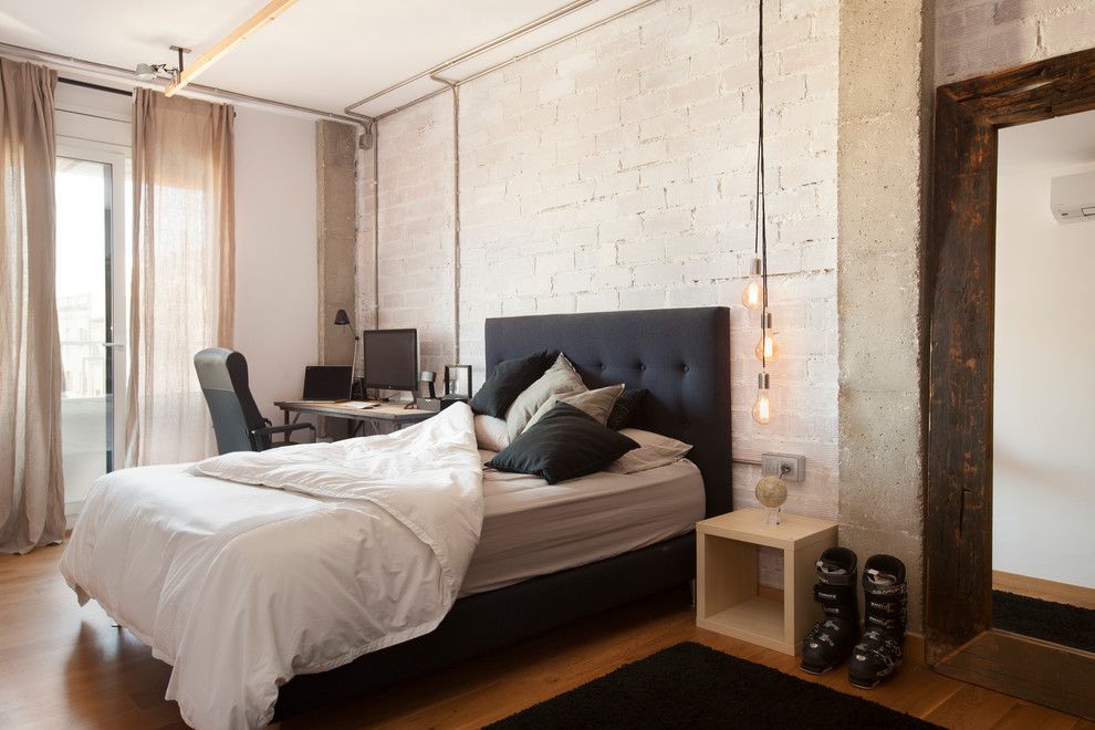 Large industrial master bedroom in Barcelona with white walls, medium hardwood floors and brown floor.