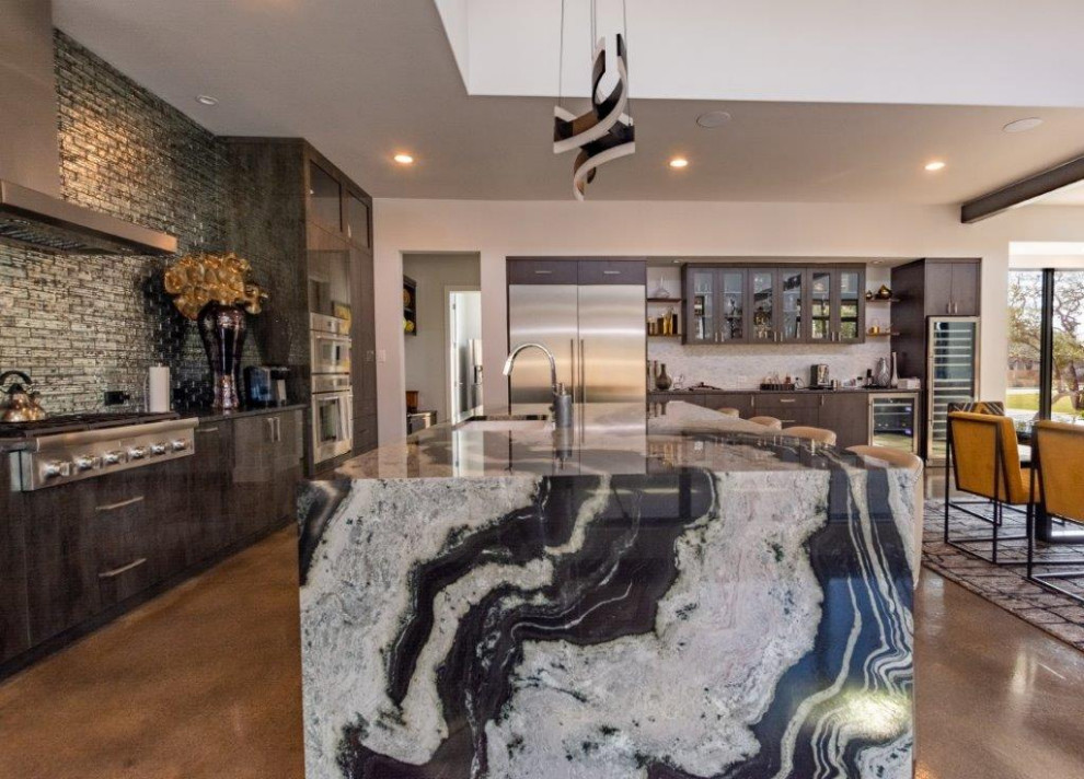 Photo of a contemporary l-shaped kitchen in Austin with an undermount sink, flat-panel cabinets, dark wood cabinets, quartz benchtops, metallic splashback, mosaic tile splashback, stainless steel appliances, concrete floors, with island, brown floor, black benchtop and recessed.