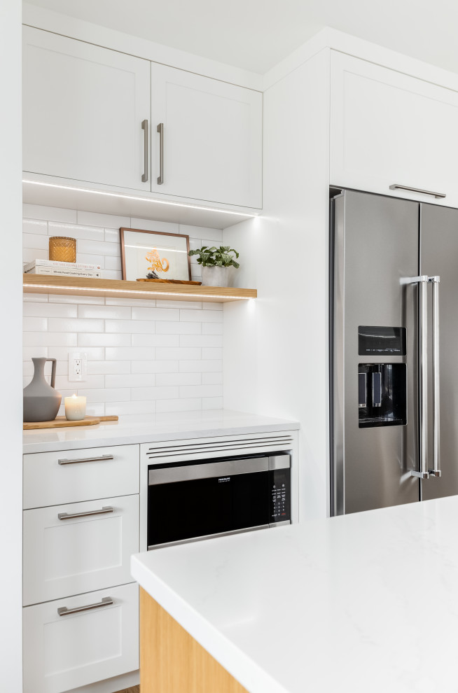 Mid-sized transitional l-shaped light wood floor and beige floor eat-in kitchen photo in Vancouver with an undermount sink, shaker cabinets, white cabinets, quartzite countertops, white backsplash, subway tile backsplash, stainless steel appliances, an island and white countertops