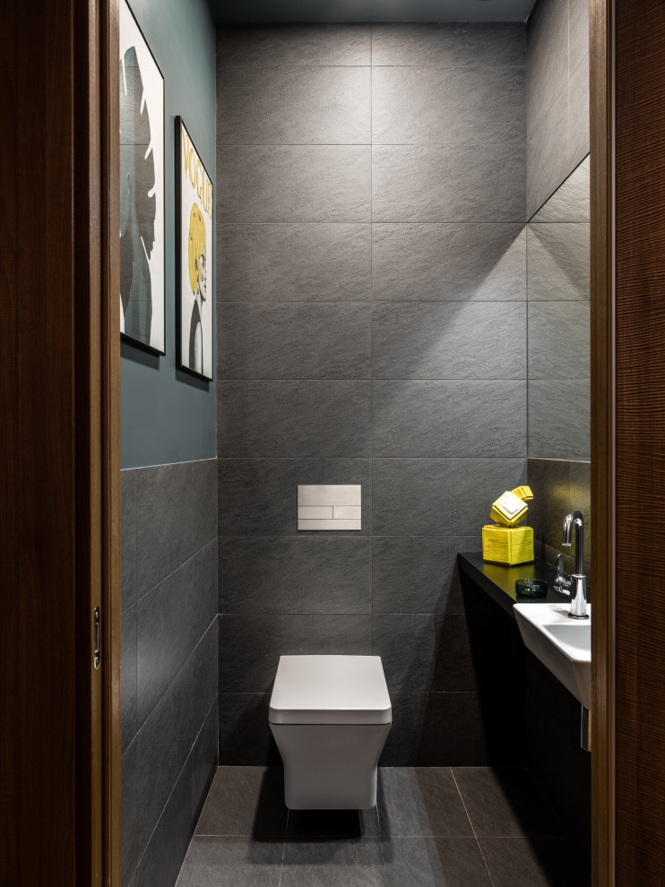 This is an example of a small contemporary powder room in Moscow with black cabinets, a one-piece toilet, gray tile, porcelain tile, green walls, porcelain floors, a wall-mount sink, wood benchtops, grey floor and black benchtops.
