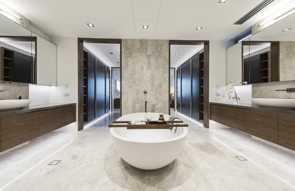 Design ideas for an expansive contemporary ensuite bathroom in Perth with recessed-panel cabinets, medium wood cabinets, a freestanding bath, beige tiles, white walls, a vessel sink, beige floors, double sinks and a floating vanity unit.