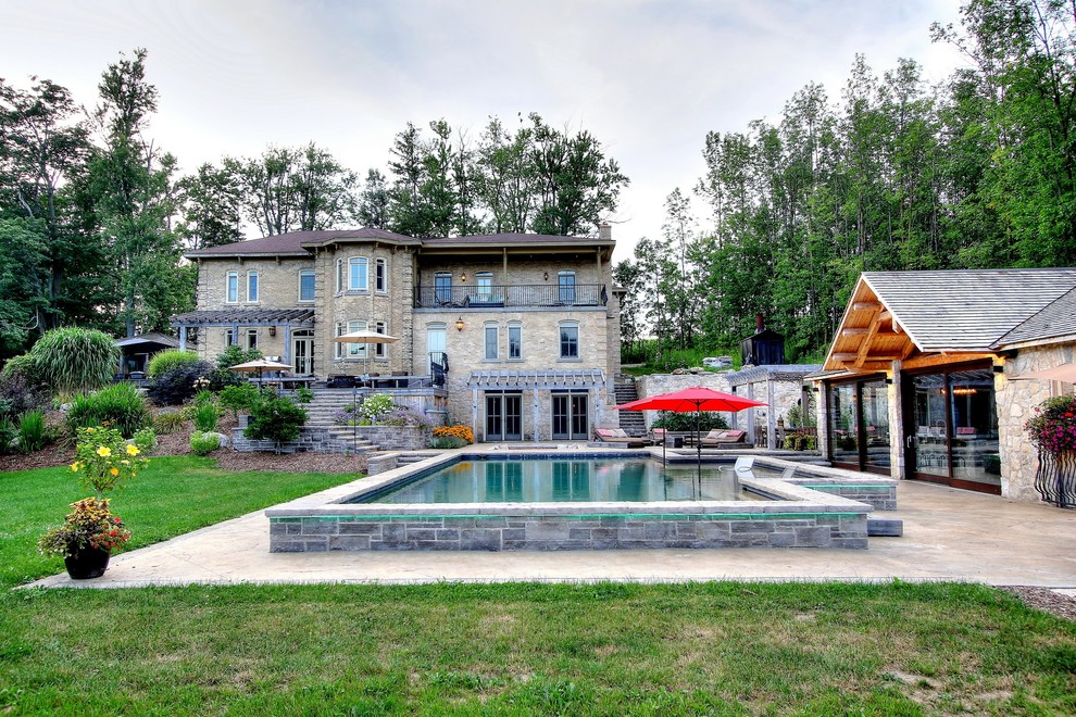 Photo of a large mediterranean front yard rectangular pool in Toronto with a pool house and stamped concrete.