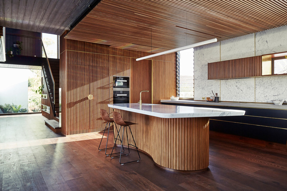 This is an example of a midcentury kitchen in Perth with a single-bowl sink, flat-panel cabinets, black cabinets, white splashback, dark hardwood floors, with island, brown floor, grey benchtop and panelled appliances.