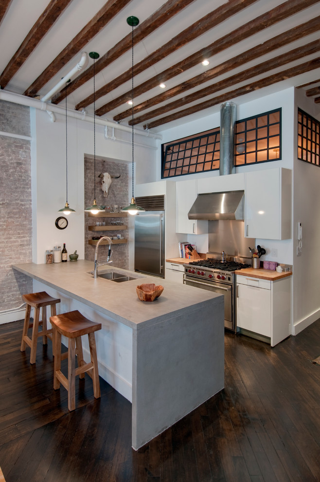 This is an example of an industrial galley kitchen in New York with concrete benchtops, stainless steel appliances, a double-bowl sink, flat-panel cabinets and white cabinets.