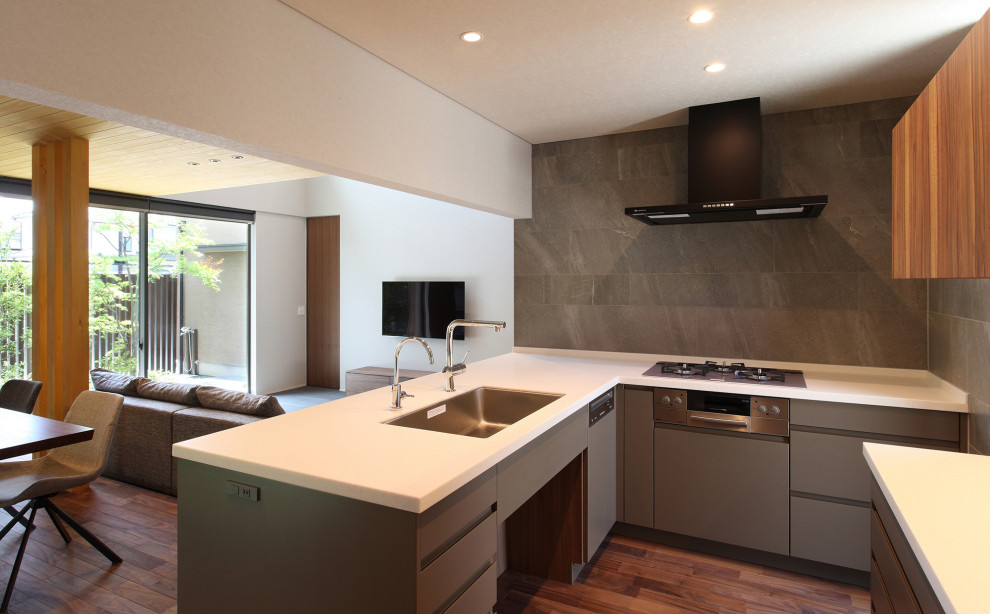 Mid-sized modern l-shaped open plan kitchen in Other with an undermount sink, beaded inset cabinets, grey cabinets, solid surface benchtops, grey splashback, ceramic splashback, black appliances, dark hardwood floors, brown floor, white benchtop and wallpaper.