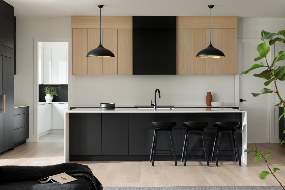 Modelo de cocina minimalista, grande, abierta, con armarios con paneles lisos, salpicadero blanco, salpicadero de azulejos de piedra, suelo de madera clara, una isla y encimeras blancas