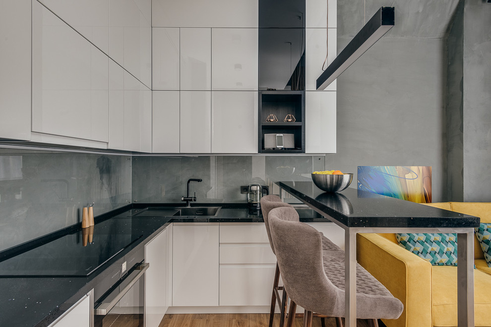 Inspiration for a contemporary l-shaped open plan kitchen in Moscow with flat-panel cabinets, white cabinets, grey splashback, glass sheet splashback, black appliances, no island, brown floor and black benchtop.