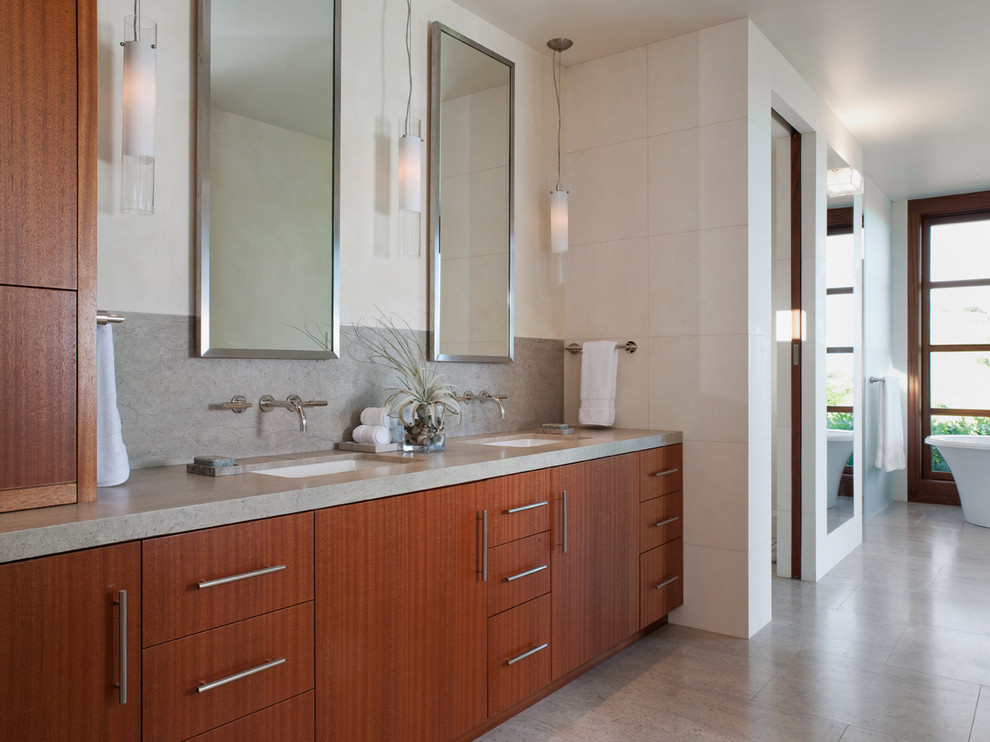 This is an example of a large contemporary master bathroom in San Francisco with an undermount sink, flat-panel cabinets, medium wood cabinets, gray tile, limestone benchtops, a freestanding tub, a double shower, a one-piece toilet, beige walls, limestone floors and limestone.