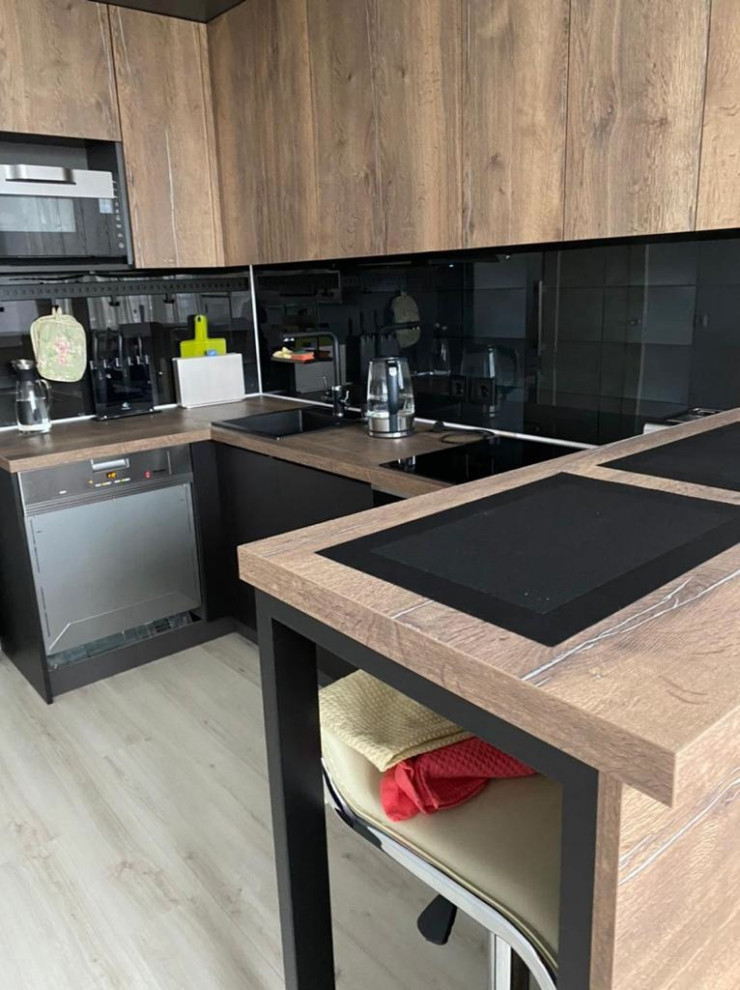 Photo of a mid-sized industrial u-shaped eat-in kitchen in Saint Petersburg with an undermount sink, flat-panel cabinets, wood benchtops, black splashback, glass tile splashback, black appliances, laminate floors and with island.