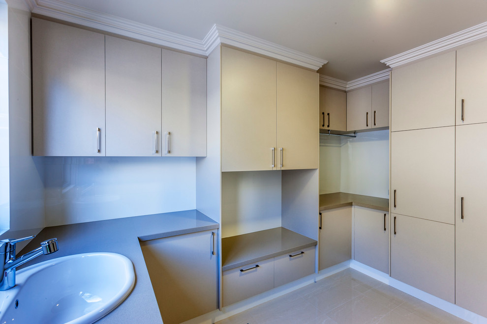 This is an example of a large contemporary dedicated laundry room in Perth with a single-bowl sink, flat-panel cabinets, beige cabinets, quartz benchtops, beige walls, porcelain floors and a side-by-side washer and dryer.