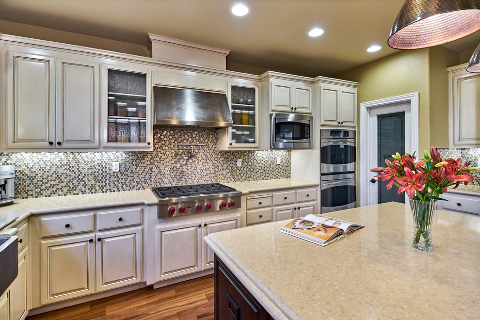 Example of a large transitional u-shaped medium tone wood floor and brown floor kitchen pantry design in San Francisco with a farmhouse sink, raised-panel cabinets, quartz countertops, stainless steel appliances, an island, beige cabinets, multicolored backsplash, mosaic tile backsplash and beige countertops