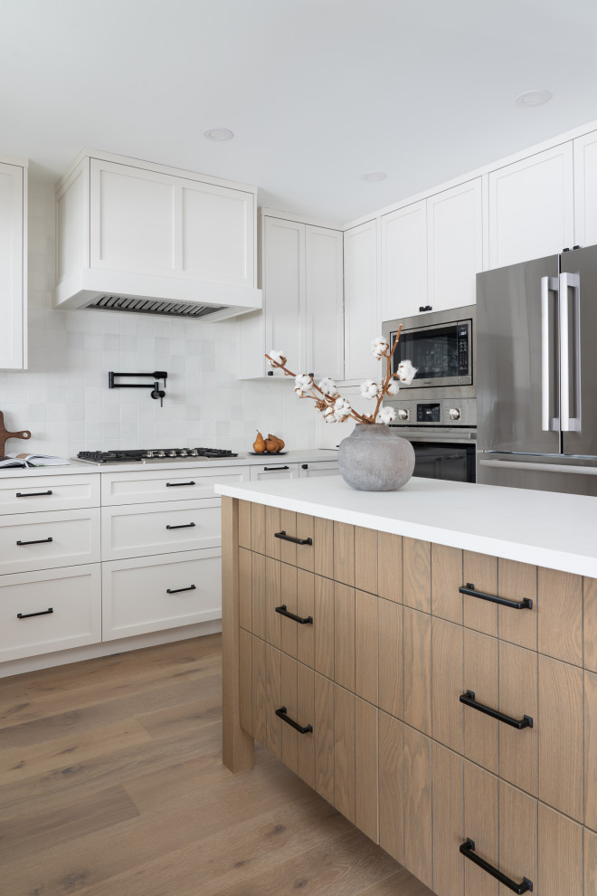 Photo of a mid-sized transitional u-shaped eat-in kitchen in Vancouver with a single-bowl sink, shaker cabinets, white cabinets, quartz benchtops, white splashback, porcelain splashback, stainless steel appliances, medium hardwood floors, with island and grey benchtop.