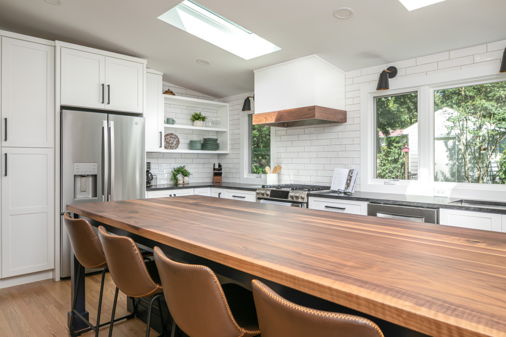 Photo of a large eclectic l-shaped eat-in kitchen in Raleigh with an undermount sink, shaker cabinets, white cabinets, wood benchtops, white splashback, porcelain splashback, stainless steel appliances, medium hardwood floors, with island, brown floor, black benchtop and vaulted.