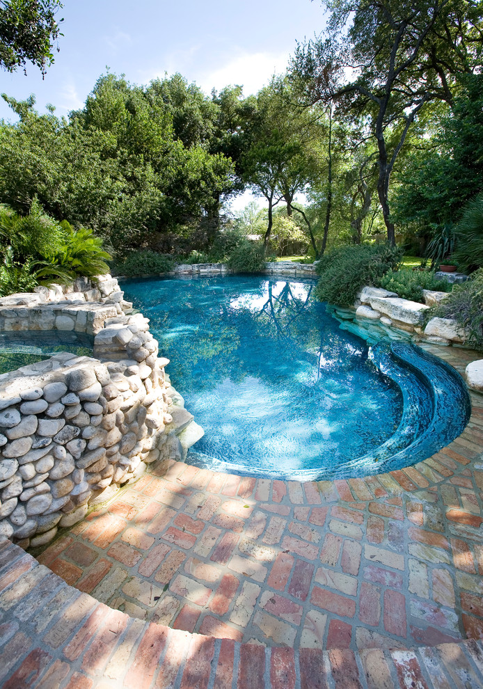 Mid-sized country backyard custom-shaped natural pool in Austin with brick pavers and a hot tub.