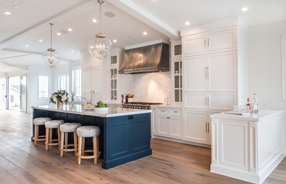 Design ideas for a large country u-shaped open plan kitchen in Los Angeles with a farmhouse sink, recessed-panel cabinets, white cabinets, solid surface benchtops, white splashback, marble splashback, panelled appliances, light hardwood floors, with island and white benchtop.
