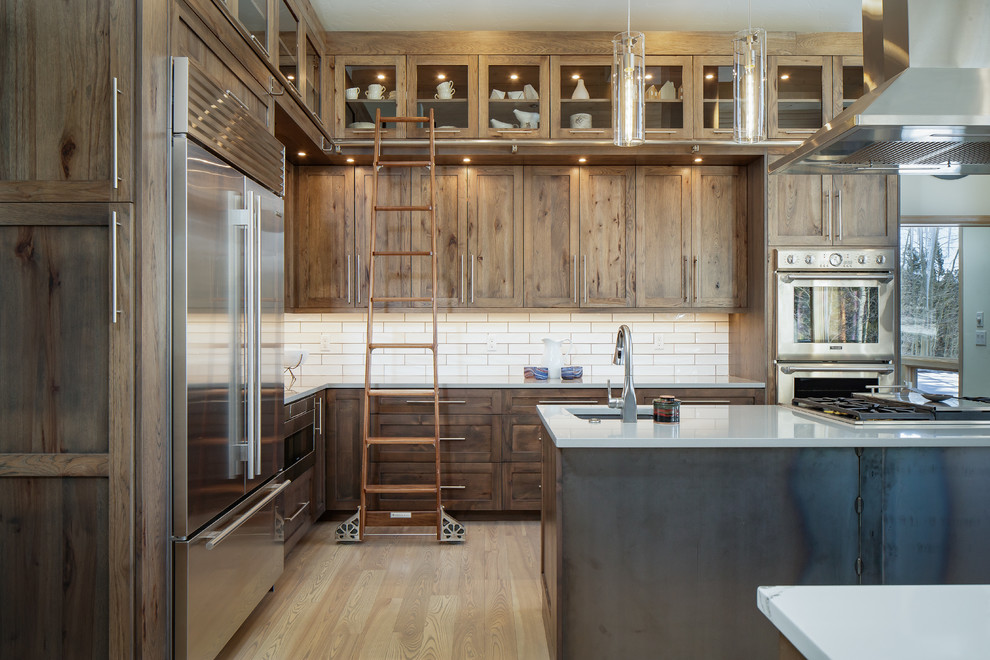 Open concept kitchen - huge transitional l-shaped light wood floor and brown floor open concept kitchen idea in Denver with an undermount sink, shaker cabinets, medium tone wood cabinets, quartz countertops, white backsplash, subway tile backsplash, stainless steel appliances, two islands and multicolored countertops
