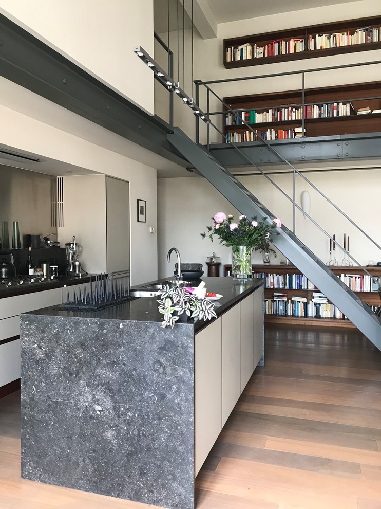 This is an example of an expansive contemporary galley open plan kitchen in Le Havre with a double-bowl sink, with island, beaded inset cabinets, white cabinets, limestone splashback, stainless steel appliances, medium hardwood floors and black benchtop.