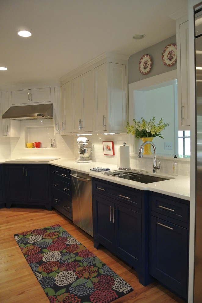 Example of a transitional l-shaped medium tone wood floor kitchen design in Boston with an undermount sink, shaker cabinets, blue cabinets, white backsplash, ceramic backsplash, stainless steel appliances and white countertops