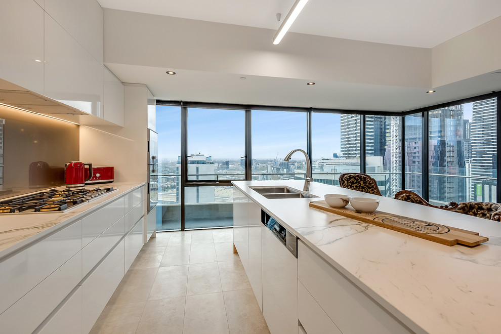 Mid-sized contemporary single-wall eat-in kitchen in Melbourne with flat-panel cabinets, white cabinets, quartz benchtops, brown splashback, glass sheet splashback, white appliances and with island.