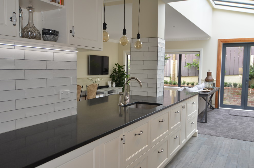 Photo of a mid-sized transitional galley eat-in kitchen in Wellington with an undermount sink, shaker cabinets, white cabinets, granite benchtops, white splashback, subway tile splashback, black appliances, ceramic floors and multi-coloured floor.