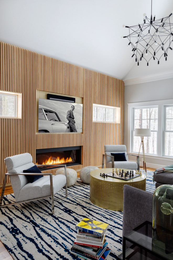 Inspiration for a contemporary living room in Boston with grey walls, medium hardwood floors, a ribbon fireplace, a wood fireplace surround, a wall-mounted tv, brown floor and wood walls.