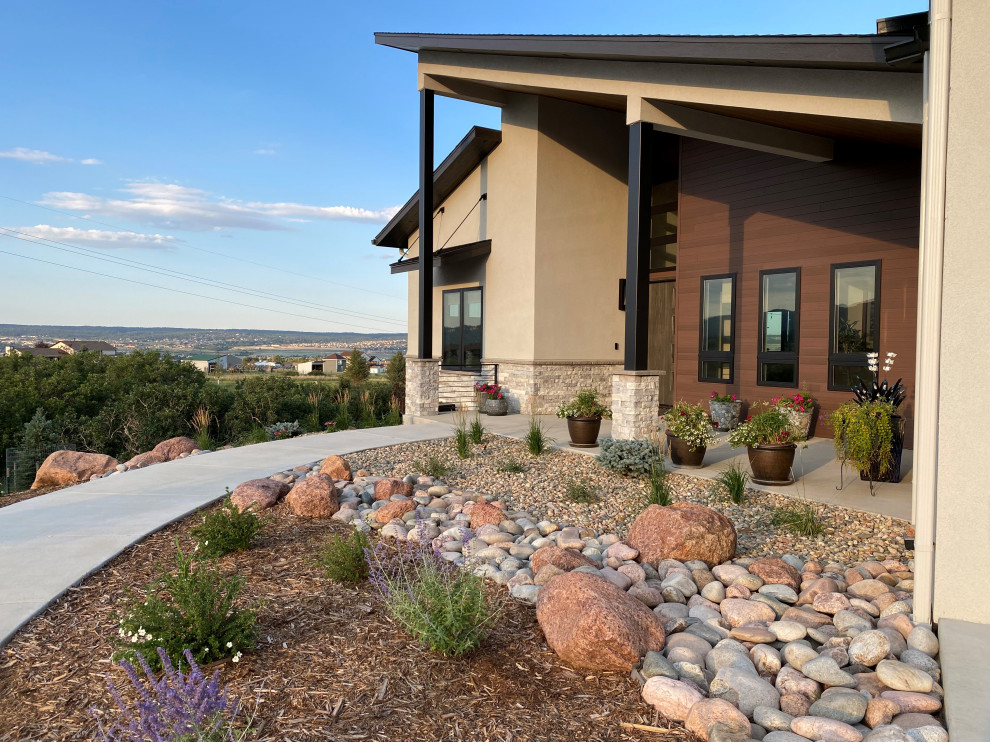 This is an example of a large contemporary front yard full sun xeriscape for spring in Denver with a garden path and river rock.