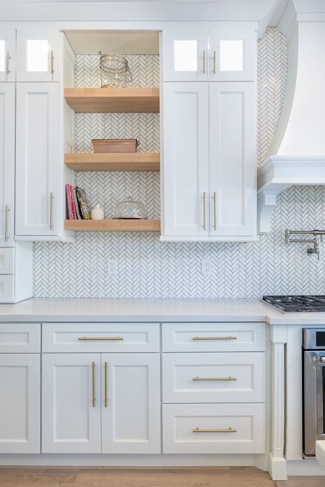 This is an example of an expansive country l-shaped eat-in kitchen in Salt Lake City with shaker cabinets, white cabinets, multi-coloured splashback, stainless steel appliances, light hardwood floors, with island, white benchtop, quartz benchtops and marble splashback.