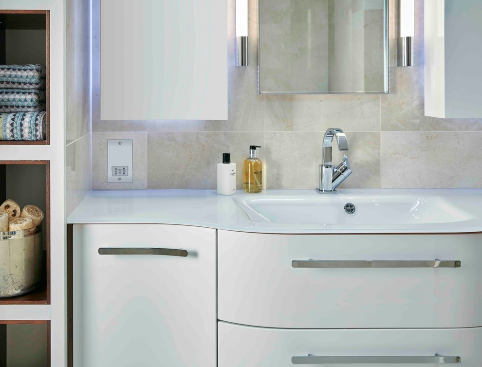 Photo of a mid-sized contemporary kids bathroom in London with flat-panel cabinets, white cabinets, beige tile and glass benchtops.
