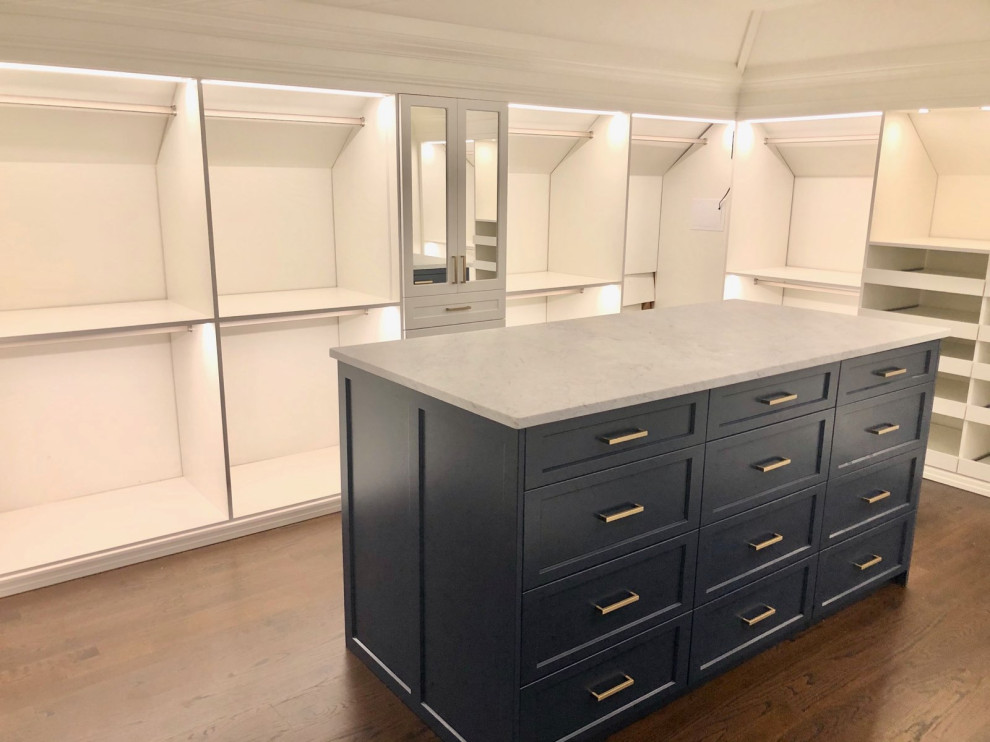 Large traditional gender-neutral walk-in wardrobe in New York with recessed-panel cabinets, blue cabinets and dark hardwood floors.