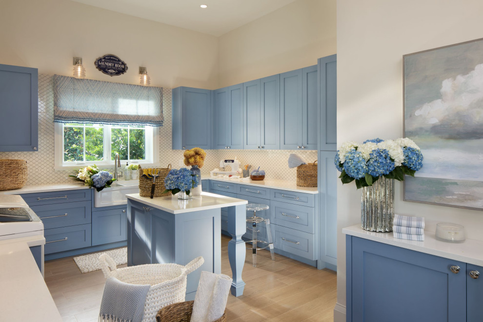 Inspiration for a mid-sized beach style galley utility room in Other with a farmhouse sink, flat-panel cabinets, blue cabinets, white splashback, ceramic splashback, white walls, marble floors and a side-by-side washer and dryer.