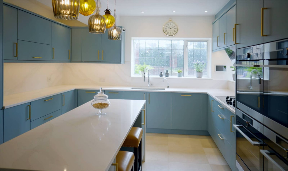 Photo of a medium sized contemporary u-shaped enclosed kitchen in Sussex with a double-bowl sink, flat-panel cabinets, blue cabinets, quartz worktops, black appliances, an island, white worktops and feature lighting.