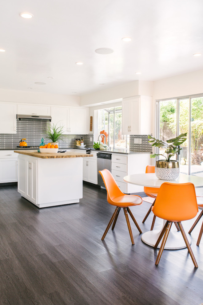 This is an example of a large midcentury l-shaped eat-in kitchen in Santa Barbara with an undermount sink, shaker cabinets, white cabinets, multi-coloured splashback, porcelain splashback, stainless steel appliances, dark hardwood floors, with island, brown floor and black benchtop.