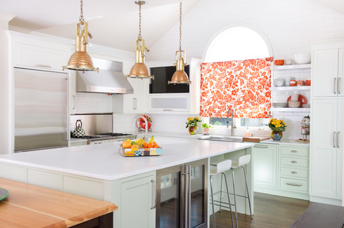 Bright white kitchen with shaker-style kitchen cabinet set, brass pendant lights, large quartz island, and an orange floral window shade.