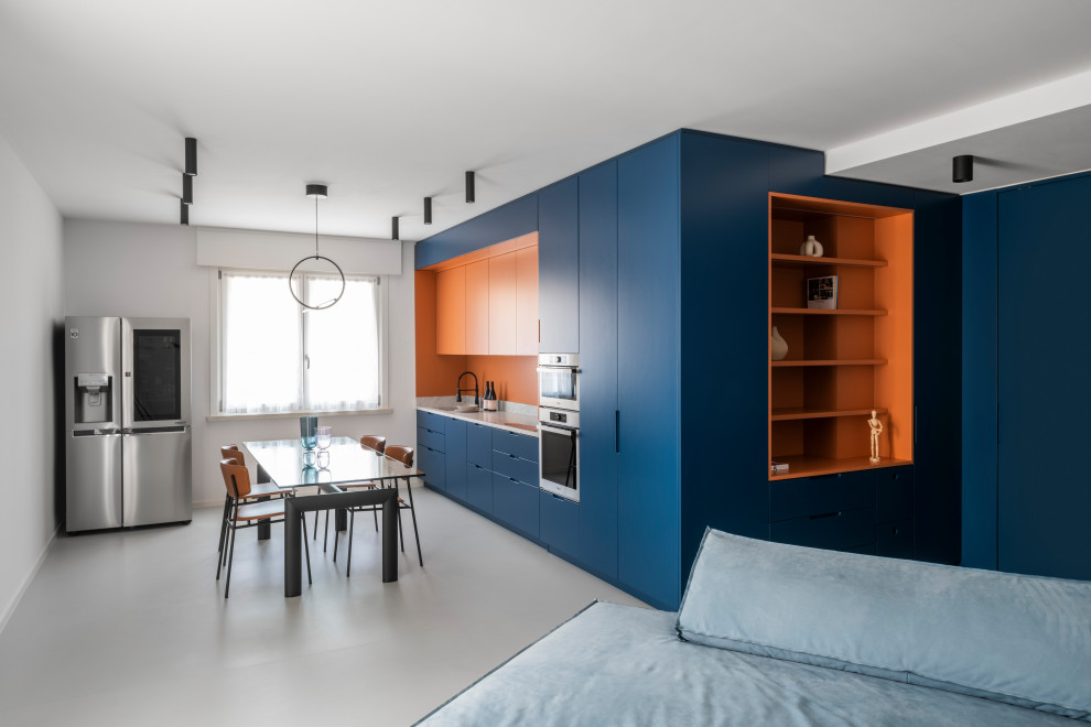 На фото: большая прямая кухня-гостиная в современном стиле с синими фасадами, мраморной столешницей, оранжевым фартуком, фартуком из мрамора, техникой из нержавеющей стали, бетонным полом, серым полом и белой столешницей