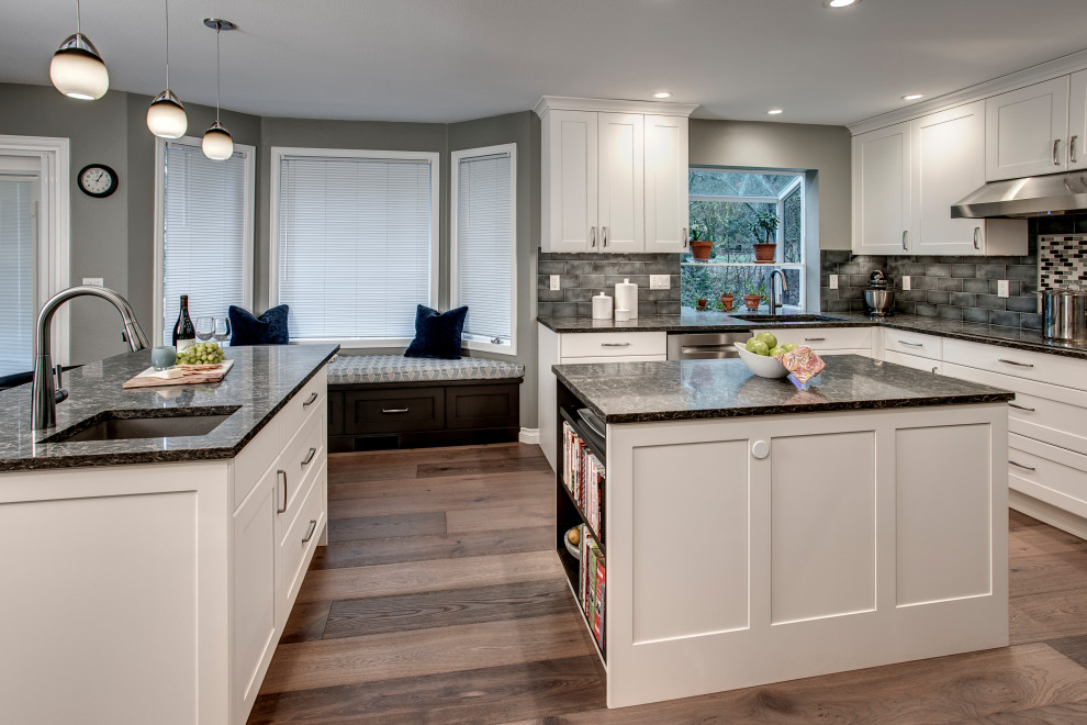 Eat-in kitchen - mid-sized transitional l-shaped medium tone wood floor and brown floor eat-in kitchen idea in Seattle with a double-bowl sink, shaker cabinets, white cabinets, quartz countertops, gray backsplash, ceramic backsplash, stainless steel appliances, two islands and gray countertops