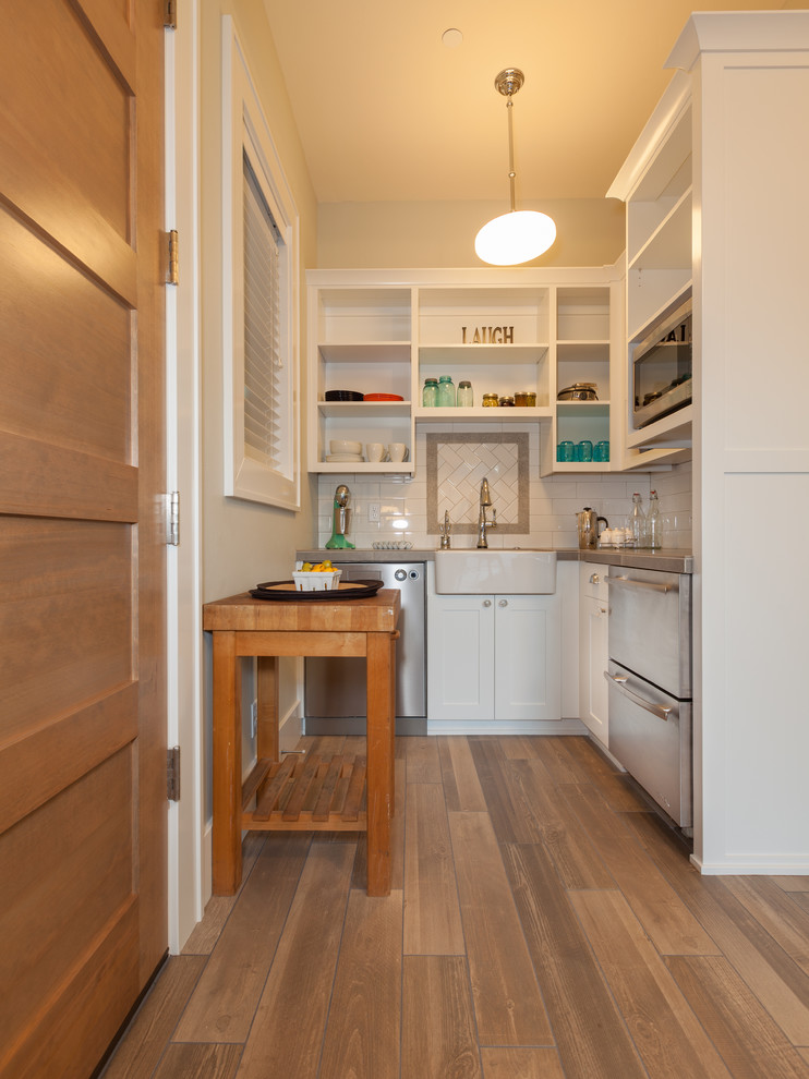 Photo of a small traditional u-shaped kitchen in Portland with a farmhouse sink, open cabinets, white cabinets, white splashback, subway tile splashback, stainless steel appliances and medium hardwood floors.