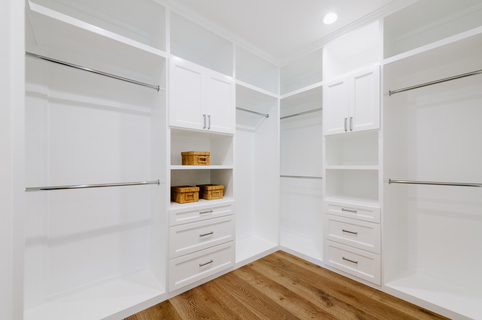 Inspiration for a large transitional gender-neutral walk-in wardrobe in Los Angeles with beaded inset cabinets, white cabinets and light hardwood floors.
