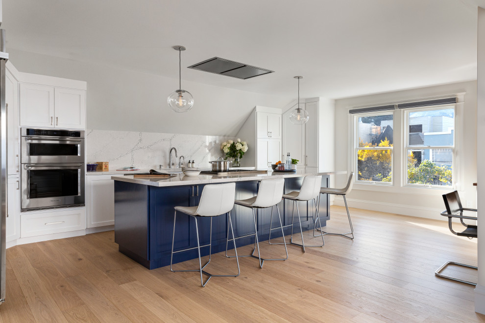 Design ideas for a large transitional galley eat-in kitchen in San Francisco with an undermount sink, shaker cabinets, blue cabinets, quartz benchtops, white splashback, engineered quartz splashback, stainless steel appliances, light hardwood floors, with island, multi-coloured floor, white benchtop and vaulted.