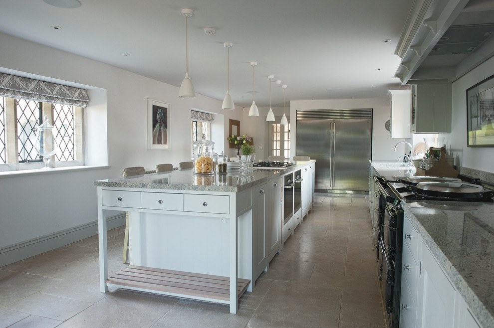Large country l-shaped separate kitchen in Gloucestershire with shaker cabinets, white cabinets, marble benchtops, stainless steel appliances, limestone floors and with island.