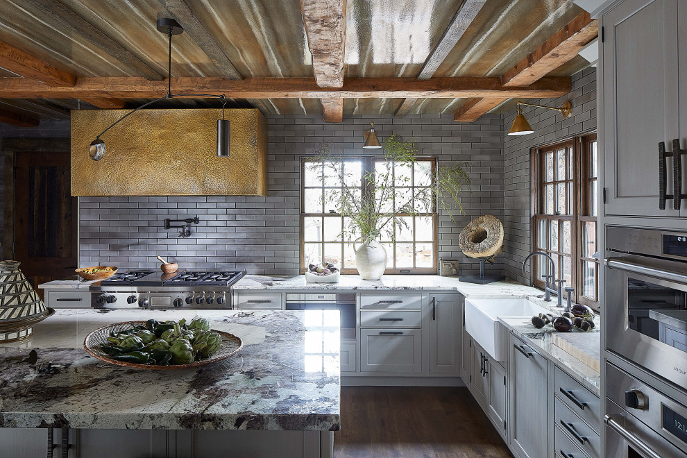 Inspiration for a rustic u-shaped dark wood floor, brown floor and exposed beam kitchen remodel in Other with a farmhouse sink, white cabinets, marble countertops, gray backsplash, subway tile backsplash, stainless steel appliances, an island and multicolored countertops