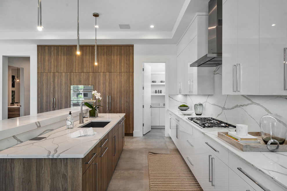Design ideas for a contemporary l-shaped kitchen in Miami with an undermount sink, flat-panel cabinets, white cabinets, white splashback, stone slab splashback, with island, grey floor and white benchtop.