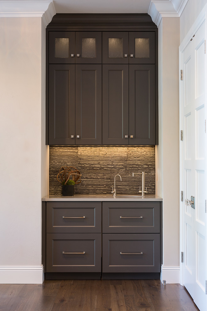 This is an example of a small transitional galley wet bar in Other with an undermount sink, recessed-panel cabinets, grey cabinets, solid surface benchtops, grey splashback, stone tile splashback and medium hardwood floors.