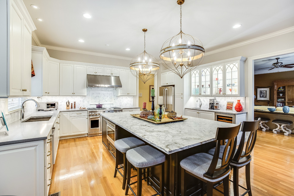 Open concept kitchen - large transitional u-shaped light wood floor and yellow floor open concept kitchen idea in Birmingham with raised-panel cabinets, white cabinets, marble countertops, white backsplash, marble backsplash, stainless steel appliances, an island and white countertops