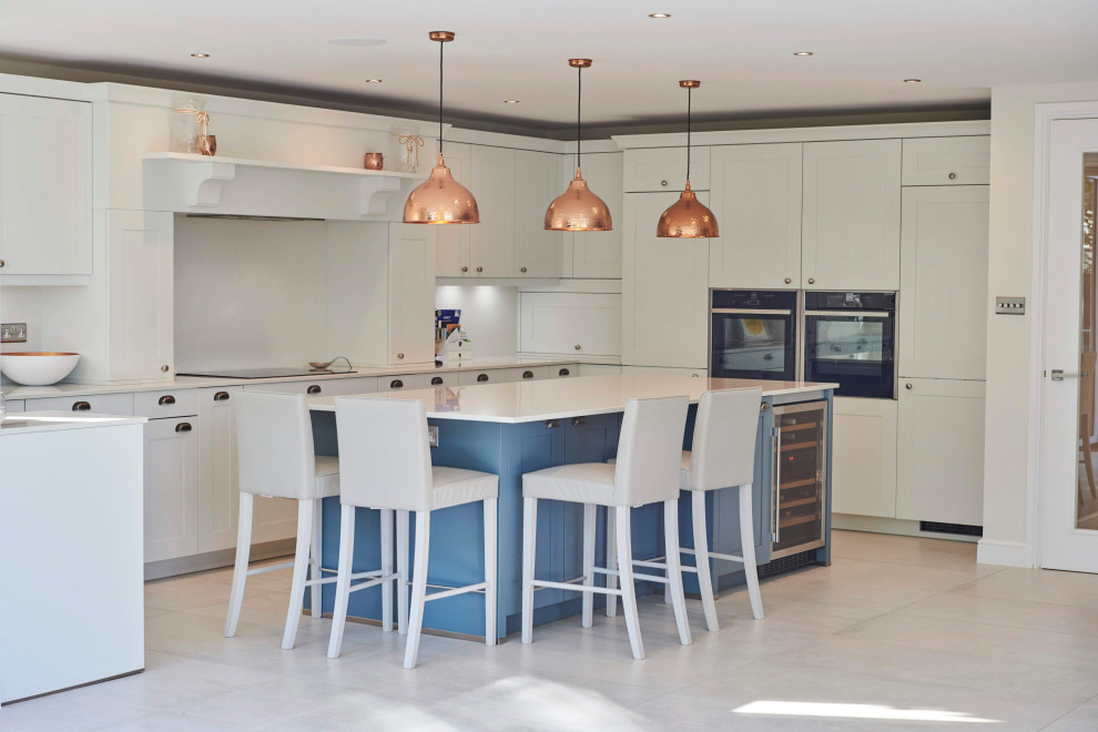 This is an example of a large traditional open plan kitchen in Other with an integrated sink, shaker cabinets, white cabinets, quartzite benchtops, white splashback, engineered quartz splashback, black appliances, porcelain floors, with island, blue floor and white benchtop.