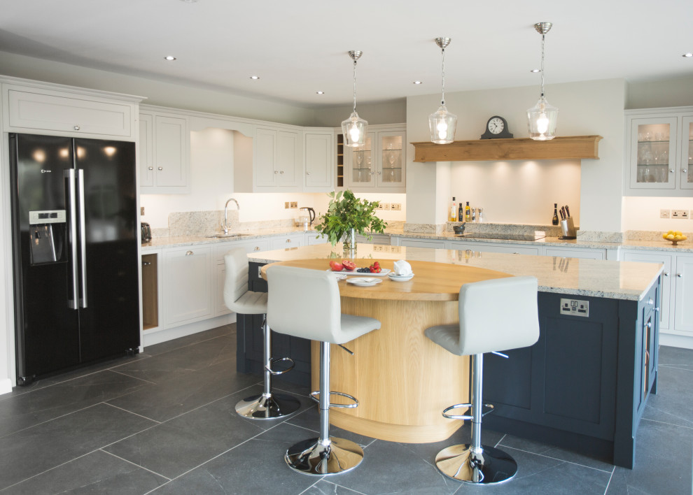 Photo of a large contemporary l-shaped enclosed kitchen with a submerged sink, shaker cabinets, grey cabinets, granite worktops, black appliances, slate flooring, an island, grey floors, beige worktops and a chimney breast.