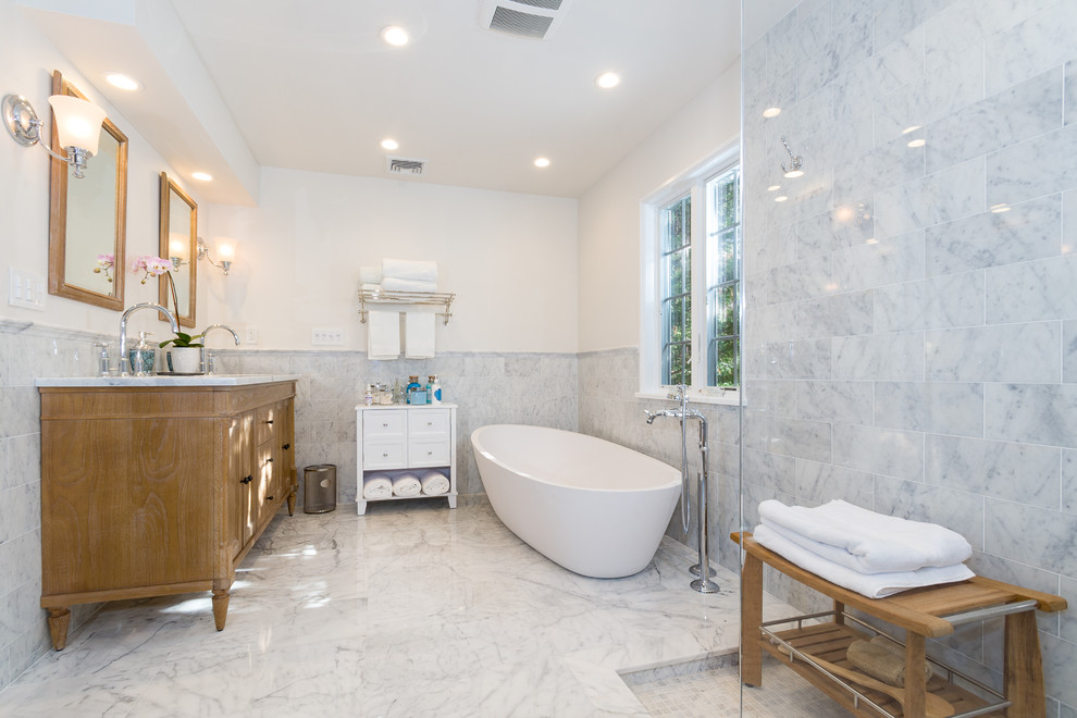 Inspiration for a large contemporary master bathroom in New York with an undermount sink, furniture-like cabinets, marble benchtops, a freestanding tub, an open shower, a one-piece toilet, white tile, stone tile, white walls, marble floors and medium wood cabinets.