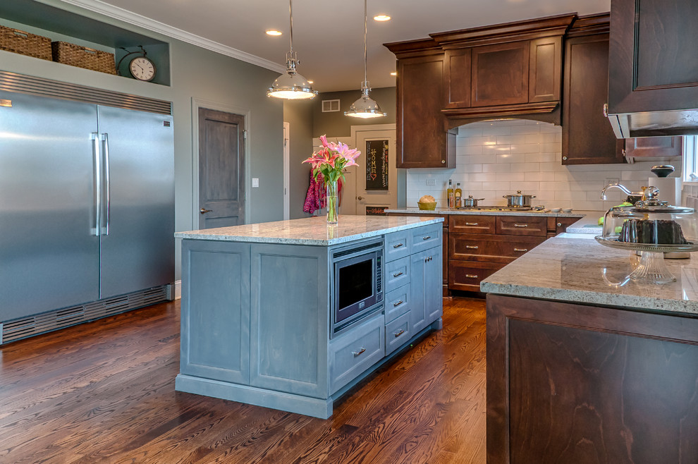 Inspiration for a mid-sized transitional u-shaped dark wood floor eat-in kitchen remodel in Chicago with a farmhouse sink, recessed-panel cabinets, medium tone wood cabinets, granite countertops, white backsplash, subway tile backsplash, stainless steel appliances and an island
