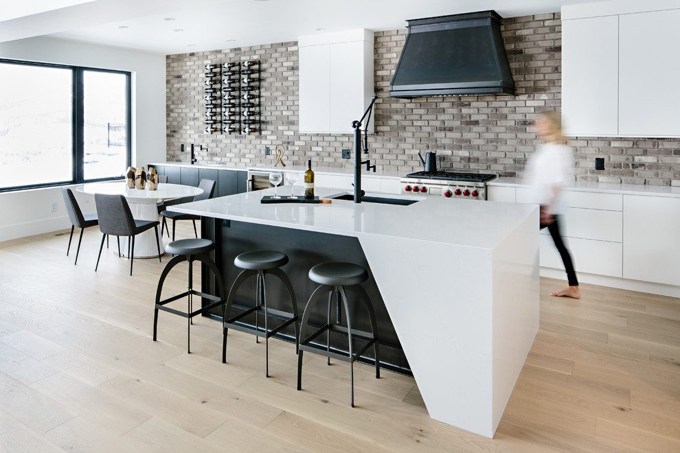 Contemporary eat-in kitchen in Other with flat-panel cabinets, brown splashback, brick splashback, stainless steel appliances, light hardwood floors, with island, an undermount sink, beige floor and white benchtop.