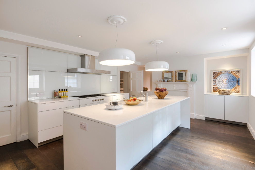 Contemporary galley kitchen in Surrey with flat-panel cabinets, white cabinets, white splashback, dark hardwood floors, with island, brown floor and white benchtop.