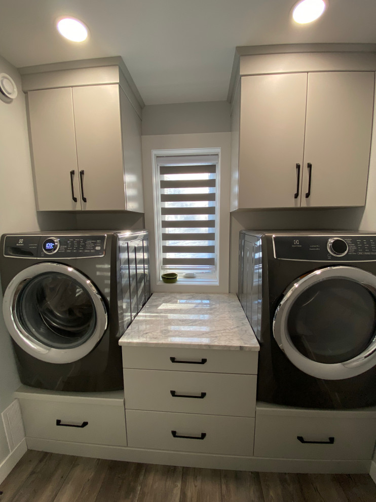 Small contemporary galley separated utility room in Calgary with flat-panel cabinets, grey cabinets, granite worktops, grey walls, vinyl flooring, a side by side washer and dryer, beige floors and white worktops.